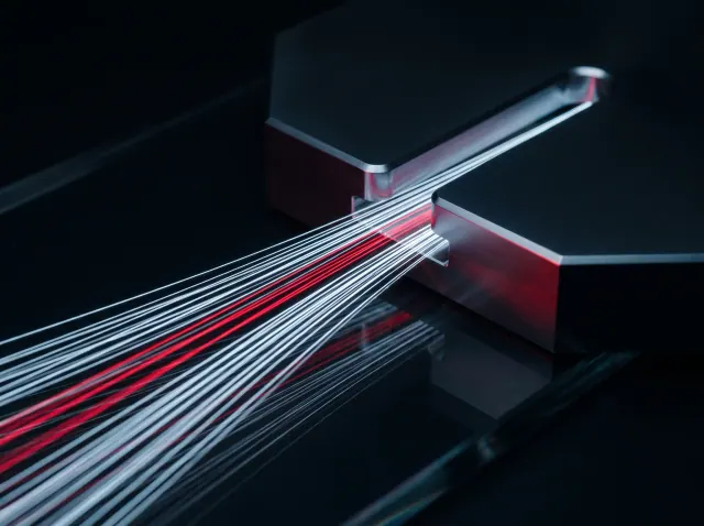 A bundle of light trails passing through a narrow slot in a dark metal plate